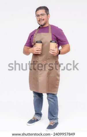 A cafe shop owner or manager presenting two cups of coffee. Wearing a purple waffle shirt and a brown apron. Full body photo, Isolated on white background. Royalty-Free Stock Photo #2409957849