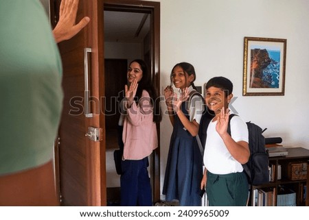 A working Indian mother and her pre-teen daughter and young son wave goodbye to their father while leaving their apartment in Mumbai, India for school and work.