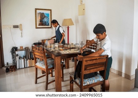 A yound Indian boy and his pre-teen sister pack their bags for school at the dinig table in their home in Mumbai before leaving the house with their mother.