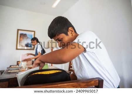 A yound Indian boy and his pre-teen sister pack their bags for school at the dinig table in their home in Mumbai before leaving the house with their mother.