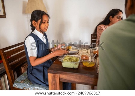 A pre-teen Indian girl, dressed in her school uniform, serves herself some chutney while eating breakfast with the family at their home in Mumbai, India.