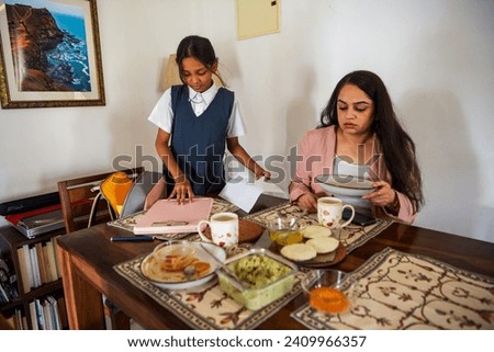 A pre-teen Indian girl packs her bag for schoool at the dining table while her mother clears her plate after breakfast at their home in Mumbai, India.