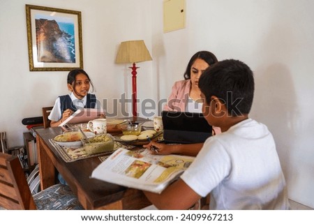 A pre-teen Indian girl and her younger brother do their homework and joke with one another while their mother is busy on a conference call, while eating breakfast at their home in Mumbai, India.