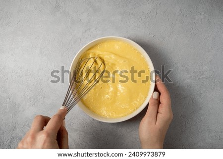 Cooking omelette. Mixing milk with melted butter and eggs using a hand whisk, top view. Royalty-Free Stock Photo #2409973879