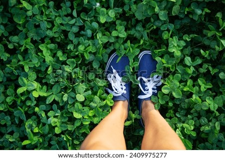 A person standing on lush green clover field. The person is wearing sneakers and the view is from the top. The image is perfect for nature, outdoor, and healthy living themes