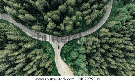 Birds eye view onto a car stopping at a crossing on a curvy road through the forest Royalty-Free Stock Photo #2409979331