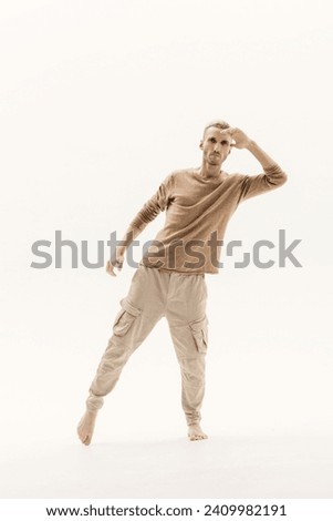 A young man in a beige jumper and cargo pants on a white background. Royalty-Free Stock Photo #2409982191