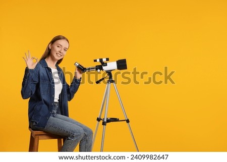 Happy astronomer with telescope showing OK gesture on orange background, space for text
