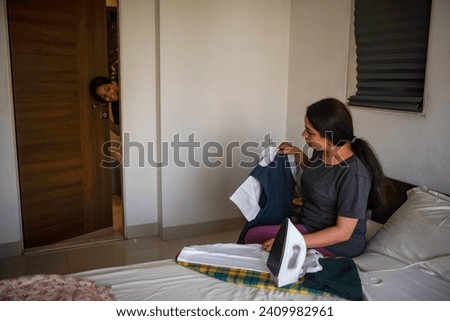 A pre-teen Indian girl calls out to her mother from the bathroom while her mother holds up an ironed school uniform at their home in Mumbai, India.