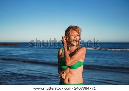 Happy senior latin woman smiling on camera during summer travel vacation on the beach