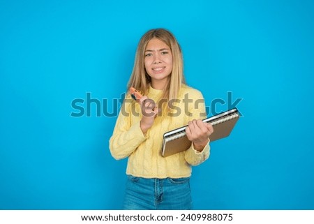 Afraid funny Caucasian teenager girl wearing yellow knitted sweater holding telephone and bitting nails
