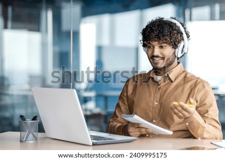 Businessman is studying inside the office, man is upgrading his qualifications, watching online video course, recording data, worker in headphones, talking, using video call. Royalty-Free Stock Photo #2409995175