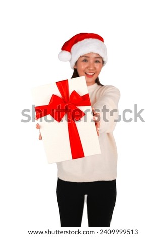 Cute young asian woman smiling while holding a gift and wearing a Christmas hat against a white background