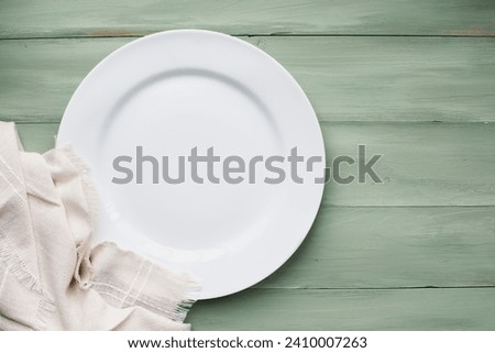 An empty white plate with napkin over a rustic green spring table, shot from flat lay or table top view position. Free space for text.
