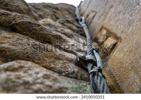 Shallow focus of a church tower lightning conductor wire seen screwed into the side of the stone work surface.