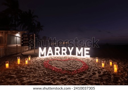 Marry me proposal decoration lights with heart shaped flower petals on sand Royalty-Free Stock Photo #2410037305