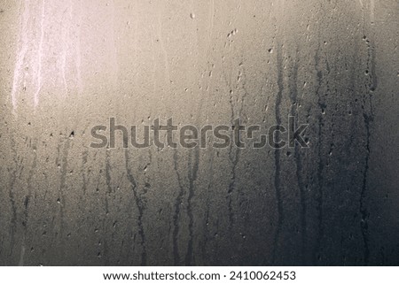 Foggy glass with drops and streaks of water. There are brightly sunlit and dark areas of the surface. Close-up. Texture. Royalty-Free Stock Photo #2410062453