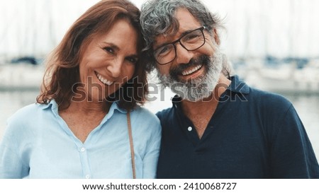 Close up, happy elderly couple hugging each other while standing in the port on the yacht background turn their heads and look at the camera with smile Royalty-Free Stock Photo #2410068727