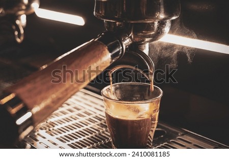 Dark tone picture for coffee cafe bar. Close-up an espresso coffee pouring from professional coffee brew machine into a cup with hot stream above the cup.
