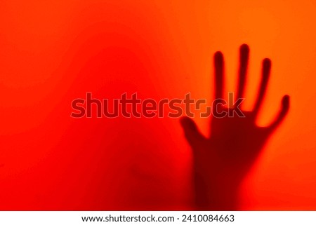 horror picture with a scary ghost like hand silhouette on an orange red background with a copy space, concept of an allien reaching out for you!