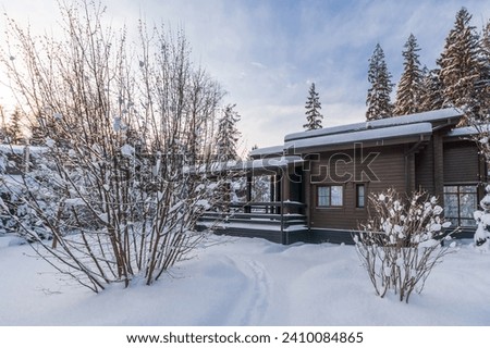 A magnificent view of a wooden house with a terrace against the background of a snowy 
landscape and blue sky.