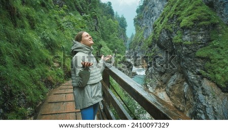 Woman enjoys the rain while hiking in a rocky gorge with mountain fast flowing river. Narrow wooden staircase along the canyon in Austria. Royalty-Free Stock Photo #2410097329