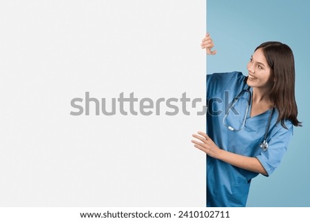 Cheerful nurse in blue attire playfully peeks around large blank sign, perfect for healthcare information or advertising on a blue background, free space