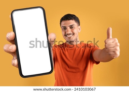Great offer. Cheerful brazilian man in casual holding huge phone with white blank screen and showing thumb up, recommending online shopping and easy fast banking, orange studio background