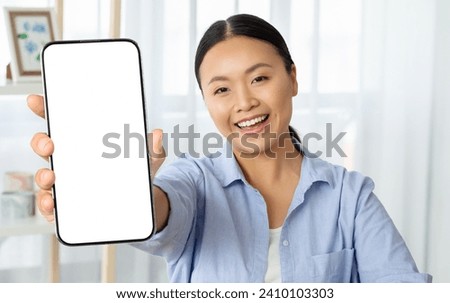Cheerful asian woman holding phone with white blank screen mockup copy space, home interior. Happy asian lady using nice mobile app, shopping, banking online, websurfing, scrolling Royalty-Free Stock Photo #2410103303