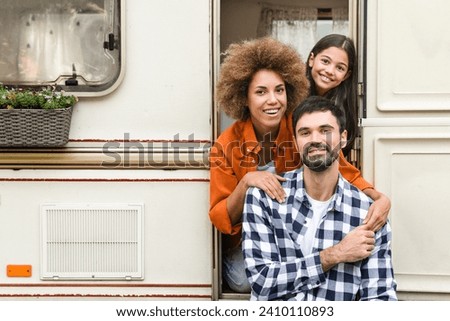 Portrait of happy family of tree with parents and small daughter traveling together by trailer motor home van home on wheels, caravanning looking at camera