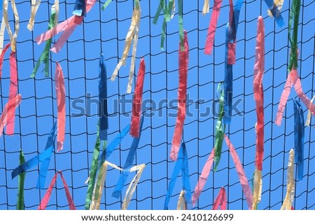 The view on the decorative mesh with multicolored paper stripes  waving on the wind and blue sky on the background 