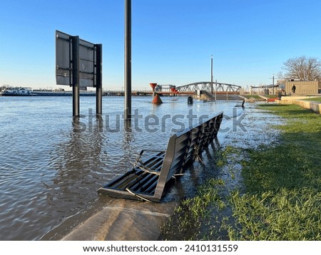 Panoramic view of flooded countenance boulevard of Zutphen with high water level of river IJssel and barrier fence under water at sunset. Royalty-Free Stock Photo #2410131559