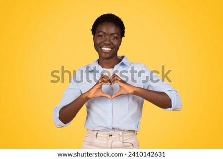 A black woman student creating a heart sign with her hands, her expression radiating joy and love, on yellow background, encapsulating warmth, positivity, and a loving academic spirit