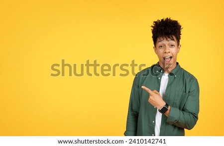 Excited handsome stylish millennial african american guy pointing at copy space and grimacing, showing mockup for advertisement, isolated on yellow studio background, banner