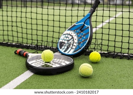 Blue padel racket and yellow balls placed on court near net on sunny day Royalty-Free Stock Photo #2410182017