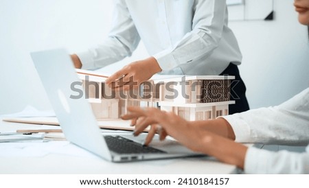 Closeup image of professional male architect hand using ruler to measure house model length while young beautiful caucasian coworker using laptop to analyzed data on meeting table with house model