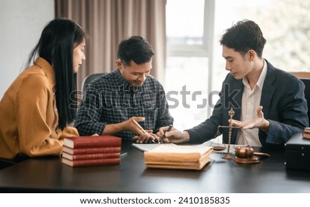 Asian legal team in meeting. woman and two men discussing over documents with law books and gavel on the table, indicating legal setting.