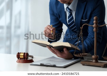 Lawyer, legal advisor, businessman reading and using pen pointing at legal code information Business terms on books working with scales and hammers in office.