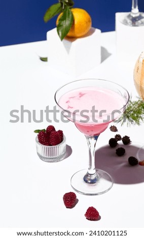 A delicate raspberry margarita cocktail, accented with fresh raspberries and pine cone decor on a geometric white stand. Royalty-Free Stock Photo #2410201125