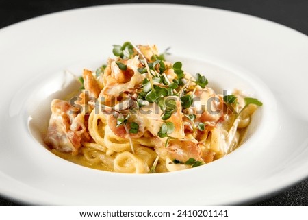 Classic carbonara pasta with a creamy sauce and garnished with fresh herbs, presented on a white plate. Royalty-Free Stock Photo #2410201141