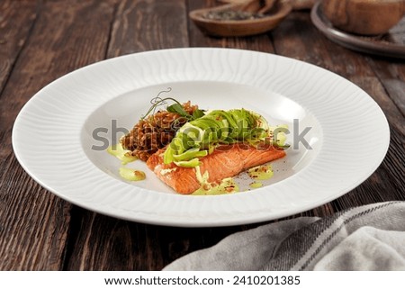Grilled salmon steak with zucchini ribbons and wild rice on a white plate, rustic wooden backdrop.