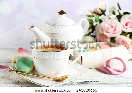 Colorful macaroons with cup of tea on color wooden table, on light background