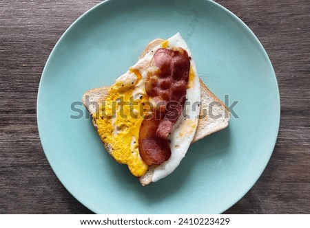 Close up top view of a visual photo of a yummy tasty delicious bacon and egg sandwish in. agreen plate on a wood table in a kitchen for breakfast in teh morning