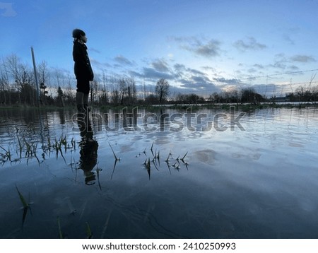 Exterior photo view of a 13 years old male boy who is looking alone at floods on field and road in Normandy during winter rains season during the day
