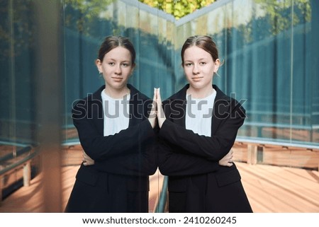 A stylish beautiful young girl stands near the mirror surface in the park. The reflection of the girl in the glass. Mirror Maze
