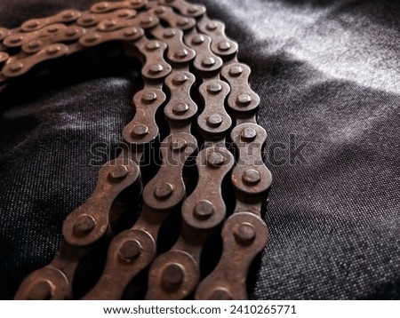 Old, aged, broken, and weathered motorbike chain on black fabric background