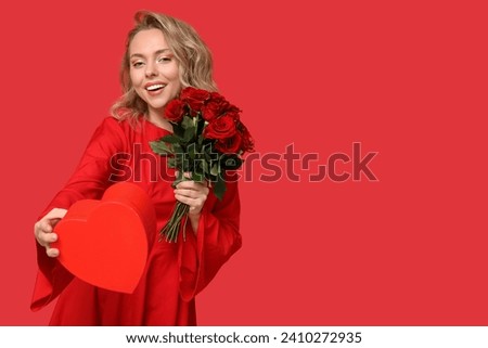 Happy young woman with bouquet of beautiful roses and gift box on red background