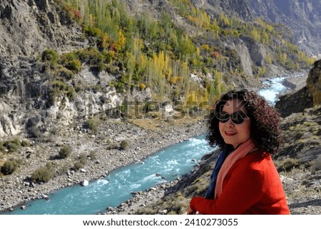 An Asian female tourist taking a picture with the view of the beautiful gorge and foliage with leaves changing colors in Hunza Valley in Gilgit-Baltistan, Pakistan.