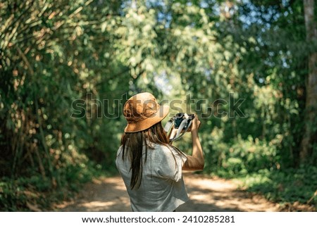 Calm young female traveler in casual summer clothes taking photo of green trees on photo camera while exploring nature