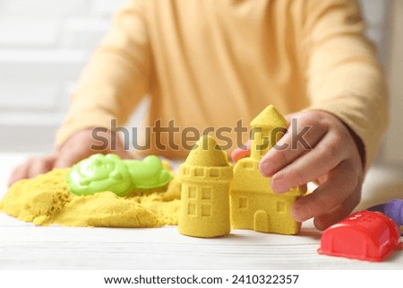 Little child playing with yellow kinetic sand at white wooden table, closeup Royalty-Free Stock Photo #2410322357